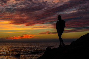The silhouette of girl that standing on the stone near the sea