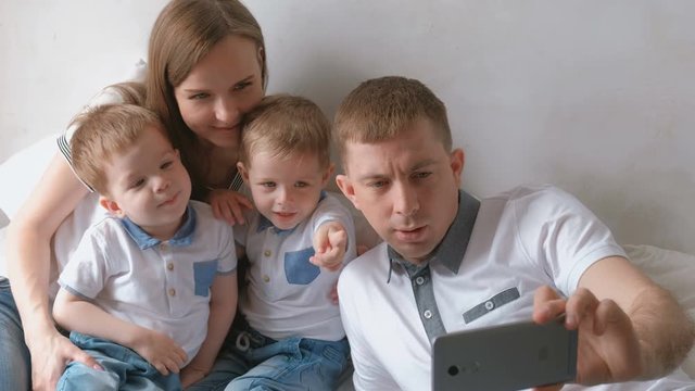 Dad makes family selfie on mobile phone. Mom, dad and two brother twins toddlers.