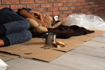 Poor homeless boy sleeping with his toy on floor near brick wall