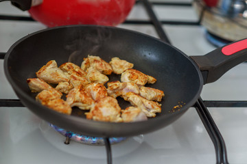 Several pieces of chopped up chicken breast with spices browned in a frying pan on stove in home.