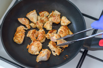 Several pieces of chopped up chicken breast with spices browned in a frying pan.Top view of cropped shot of man cooking poultry in frying pan on stove in home.
