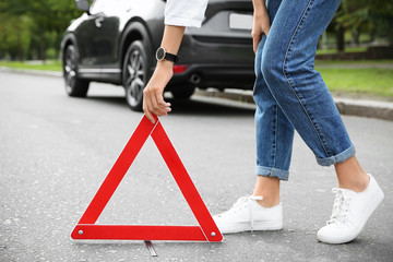 Woman putting emergency stop sign near broken car, closeup