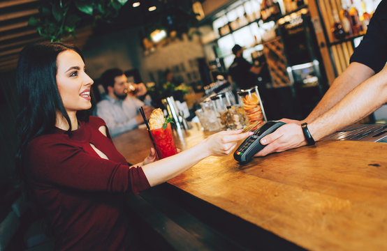 A picture of stunning girl sitting close to barman and paying for her order. She gives a credit card to barman to pay for that.