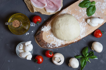 Raw dough for pizza with ingredients: mushrooms, tomatoes, ham, mozzarella, oil, basil on table