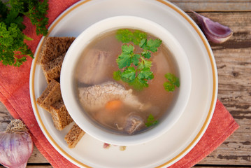 Clear beef broth, bouillon in white bowl and vegetables on wooden table. Rustic style. Top view.