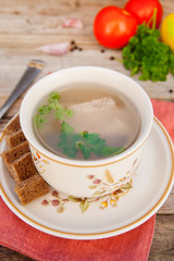 Clear beef broth, bouillon in white bowl and vegetables on wooden table. Rustic style.