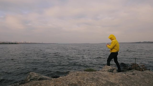Hiking traveler man in yellow jacket walking alone at river, take a picture by smartphone