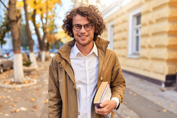 Portrait of handsome young man with books outdoors. College male student carrying books in college...