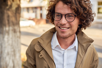 Closeup portrait of young businessman with glasses smiling and posing outdoors. College male...