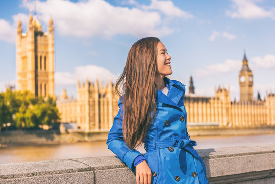 London city lifestyle Asian businesswoman Europe autumn travel in blue trench coat. Multiracial model posing in fashion fall outerwear at Westminster and Big Ben, famous european urban destination.