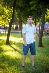Close up outdoors portrait of beautiful joyful Hispanic man in blue shirt smiling with teeth on summer nature park background. Fashion model