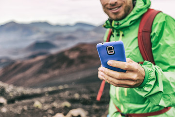 Hiker man taking photo with phone holding blue cover smartphone during outdoor activity in nature landscape. Hiking sport lifestyle young tourist on adventure.