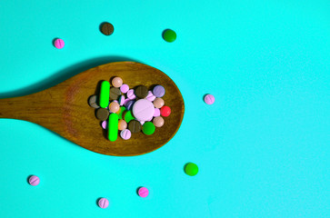 Assorted pharmaceutical medicine pills, tablets and capsules on wooden spoon. Blue background