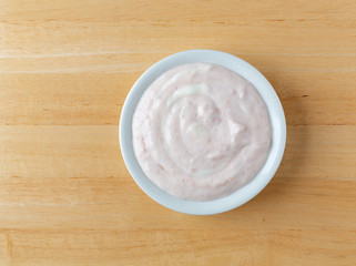 Top view of a bowl of strawberry rhubarb yogurt sweetened with honey on a wood table.