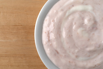 Top close view of a bowl of strawberry rhubarb yogurt sweetened with honey on a wood table.