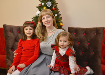 Mother with two daughters sit against the background of a New Year tree