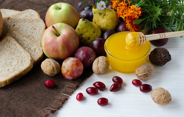 On a white wooden background is a tablecloth made of brown fabric with a new crop of honey, apples, plums, pears, carnelian, nuts and decorated with marigolds. Fruit Background