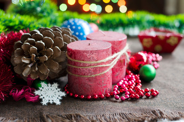 Two red candles with a large pine cone on the background of New Year's entourage (Christmas balls, busov) with blurred lights of garlands