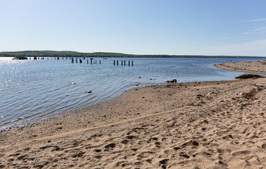 View Sandy Point Beach Park in Stockton Springs, Maine on a bright sunny morning with the remains of a pier in the distance.