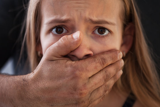 Child abuse concept - male hand covering a frightened young girl mouth