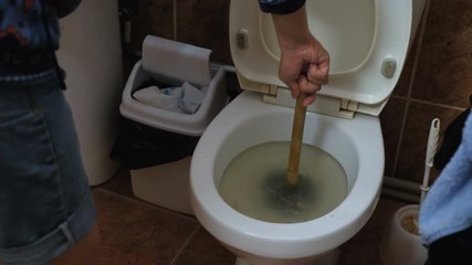 A young man is trying to eliminate the blockage in the toilet with the help of a plunger.