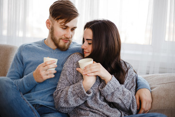 Couple in living room. Young man and woman cuddling, drinking coffee. Home weekend, rest, good morning, leisure concept