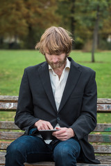 Fototapeta premium Man is using a tablet while sitting on a bench