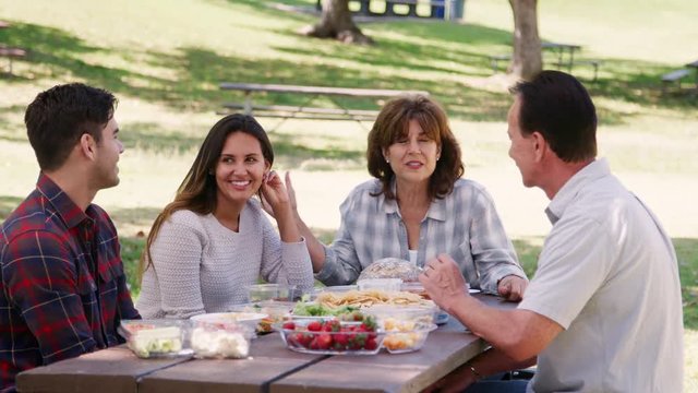 Young couple and senior couple eating at a table in park