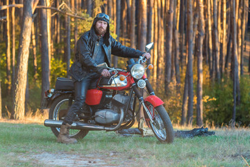 Biker in a leather jacket and helmet on a retro motorcycle in the forest