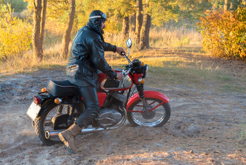 Obraz premium Biker in a leather jacket and helmet on a retro motorcycle in the forest