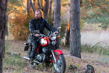 Fototapeta na wymiar Biker in a leather jacket and helmet on a retro motorcycle in the forest