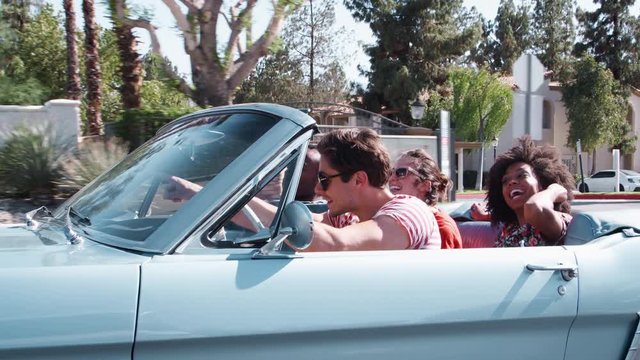 Happy young adult friends on the road in a convertible