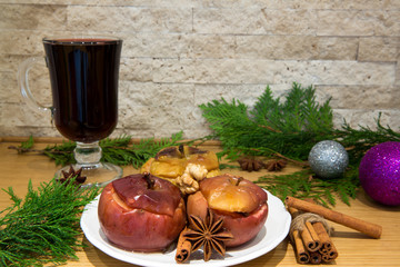 Red mulled wine and baked apples with nuts and spices, cinnamon and anise. Decorated with fir branches and christmas silver and violet balls, brick wall background.