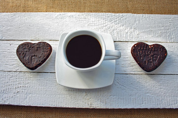 Black coffee in a white cup on a white background, chocolate gingerbread in the shape of hearts