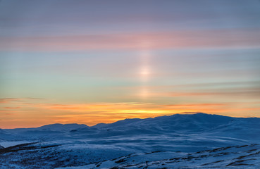 Fototapeta na wymiar Very beautiful sunset at Scandinavian mountains - red orange sun beams coloring the white snow and blue sky, sun shines up as a laser beam