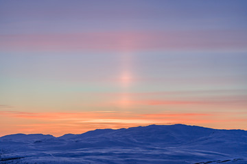 Very beautiful sunset at Scandinavian mountains - red orange sun beams coloring the white snow and blue sky