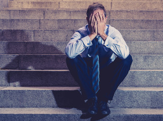 Depressed sad business man in total despair felling hopeless and frustrated sitting in city stairs