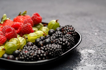 Photo of blackberry, strawberry, raspberry, gooseberry on black plate