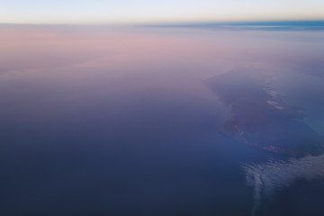 view of the earth and Lake Baikal from the window of an airplane from a height of 10,000 meters above the clouds illuminated by the rays of the rising sun