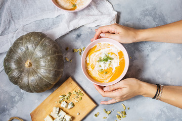 Female hands holding a bowl of pumpkin soup on concrete background.
