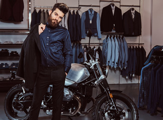 Fototapeta na wymiar Elegantly dressed man holds jacket posing near retro sports motorbike at the men's clothing store.