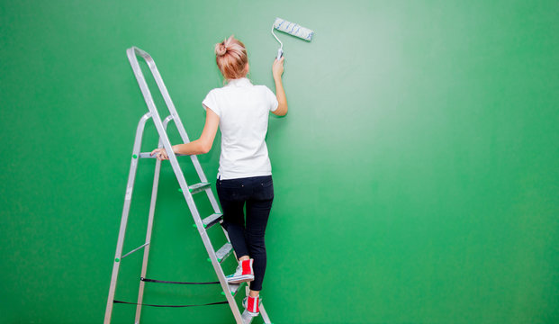 Young woman with paint roller and ladder in own house after painting a room. Real people