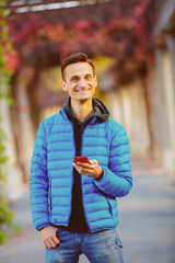 handsome tall man in blue jacket with mobile phone at alley in fall time.