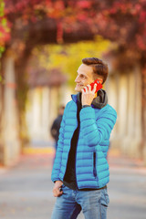 Fototapeta premium handsome tall man in blue jacket with mobile phone at alley in fall time.