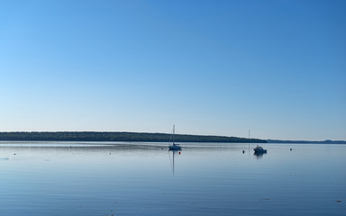 Wide view of two boats moored on Penobscot Bay at Searsport with floating seaweed in the foreground.