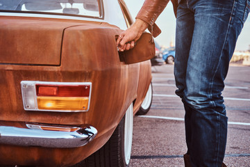 Male hand opens the gas cap of a tuned retro car for refueling.