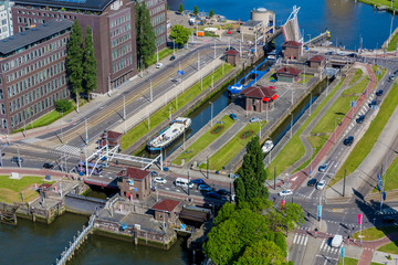 Panoramic aerial view of cargo ships sailing from one canal to another between drawbridges, buildings and streets with cars driving, sunny day in the city of Rotterdam, South Holland, Netherlands