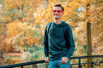 Happy man in red glasses on a bridge in a park. Autumn season time