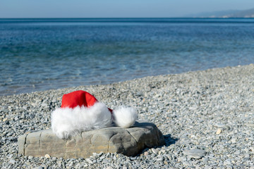 Santa Claus hat lies on a large stone on the seashore. Santa went swimming