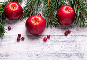 Christmas background with tree branches, red apples and cranberries. Light wooden table. Top view. Copy space